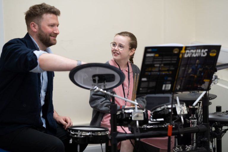 student using the drums, with a teacher helping out