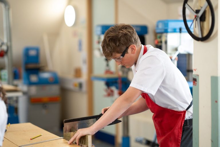 student using a hacksaw in a woodwork lesson